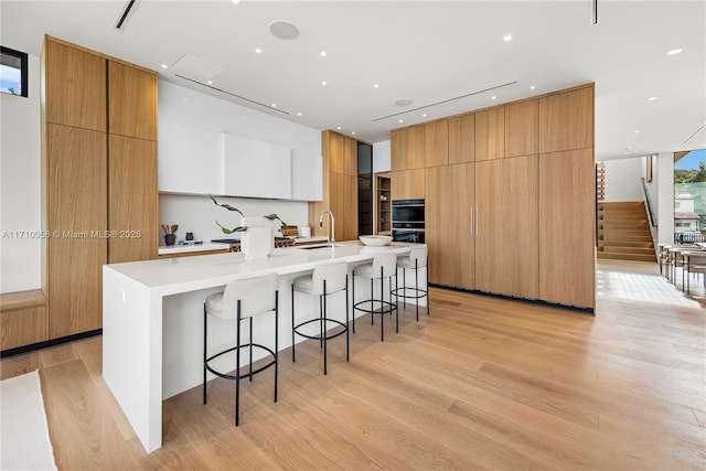 kitchen with white cabinets, sink, a large island with sink, and light hardwood / wood-style flooring