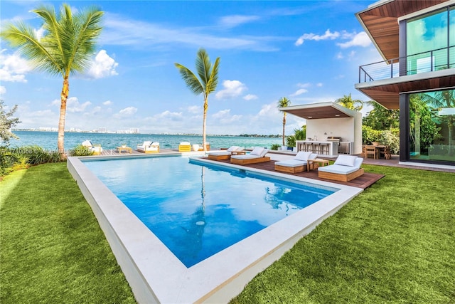 view of swimming pool with an outdoor kitchen, a water view, and a yard