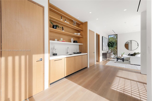 bar with a wall of windows, light wood-type flooring, sink, and light brown cabinetry