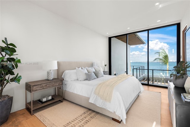 bedroom with a water view, hardwood / wood-style floors, expansive windows, and access to outside