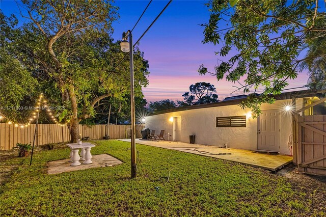 yard at dusk featuring fence and a patio