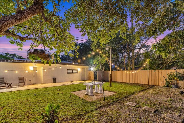 yard at dusk featuring fence and a patio
