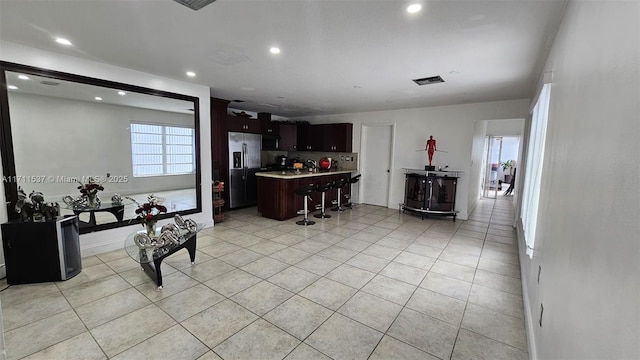 kitchen with a kitchen breakfast bar, stainless steel appliances, a kitchen island, dark brown cabinets, and light tile patterned flooring