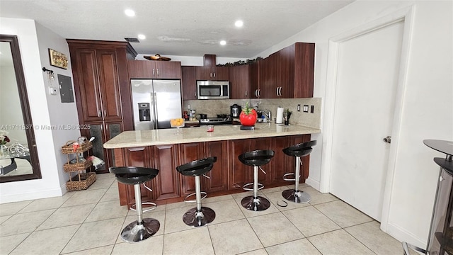 kitchen featuring light tile patterned floors, kitchen peninsula, a breakfast bar area, decorative backsplash, and appliances with stainless steel finishes