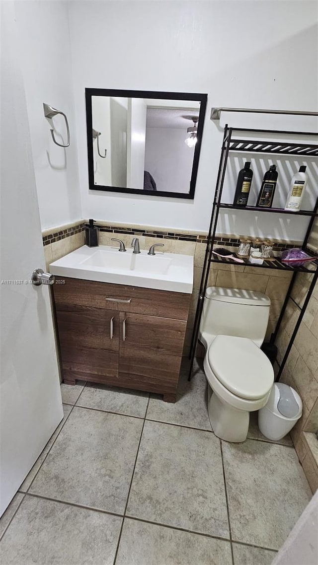 bathroom featuring toilet, tile patterned flooring, vanity, and tile walls