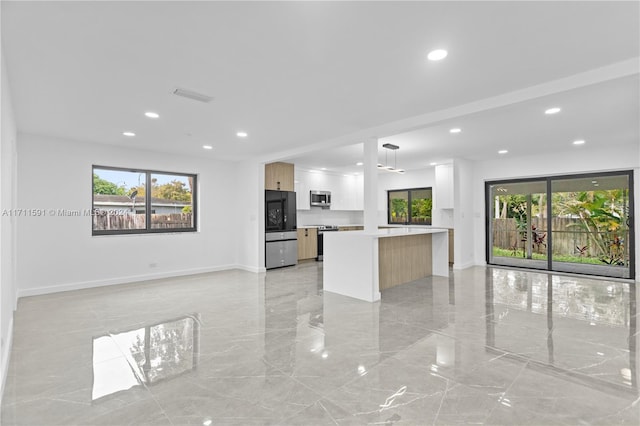 kitchen with appliances with stainless steel finishes, light brown cabinets, decorative light fixtures, a center island, and white cabinetry