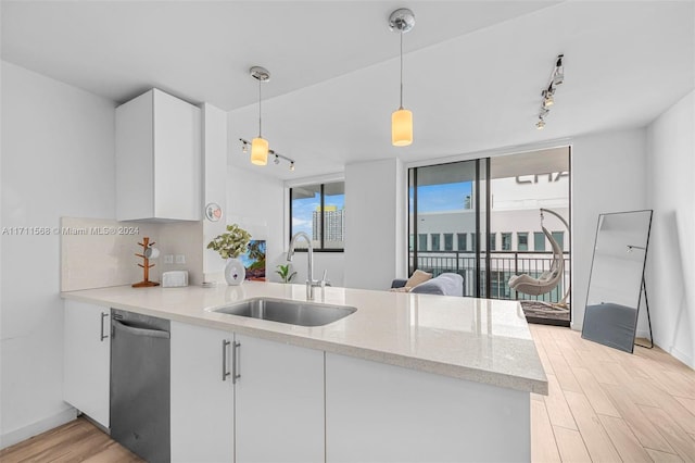 kitchen with white cabinets, sink, hanging light fixtures, light hardwood / wood-style flooring, and stainless steel dishwasher