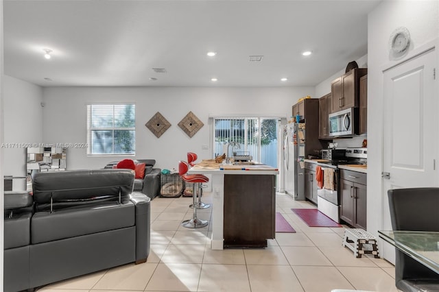 kitchen featuring dark brown cabinetry, stainless steel appliances, a kitchen breakfast bar, a kitchen island with sink, and light tile patterned floors