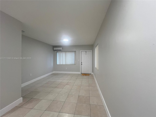 empty room featuring light tile patterned flooring, a wall mounted AC, and baseboards