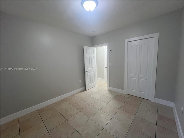 unfurnished bedroom with light tile patterned floors, a closet, and baseboards