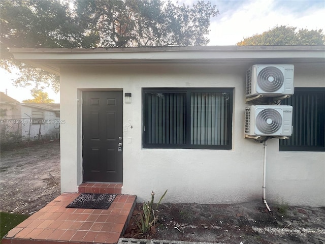 view of exterior entry with stucco siding and ac unit