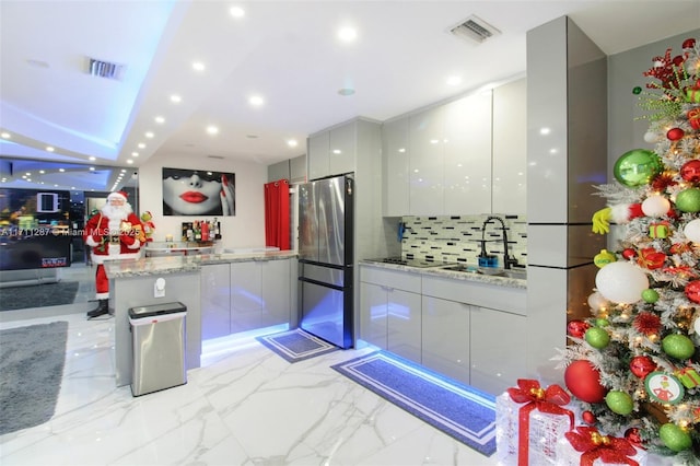 kitchen with sink, tasteful backsplash, stainless steel fridge, kitchen peninsula, and light stone countertops