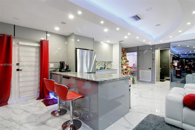 interior space featuring light stone counters, sink, a breakfast bar area, white cabinetry, and stainless steel refrigerator