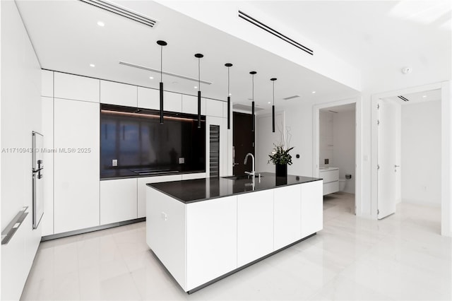 kitchen with a center island with sink, white cabinets, hanging light fixtures, and sink