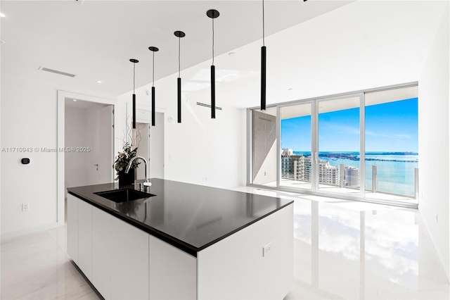 kitchen with sink, a wall of windows, white cabinets, pendant lighting, and a water view