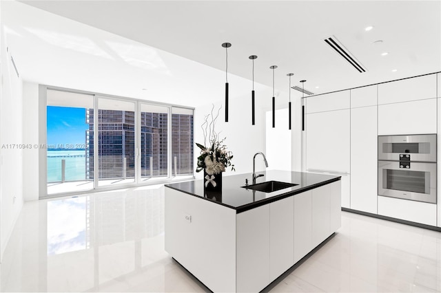 kitchen with floor to ceiling windows, sink, white cabinets, decorative light fixtures, and a water view