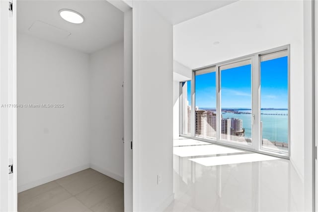 empty room with light tile patterned floors, a water view, and a wall of windows