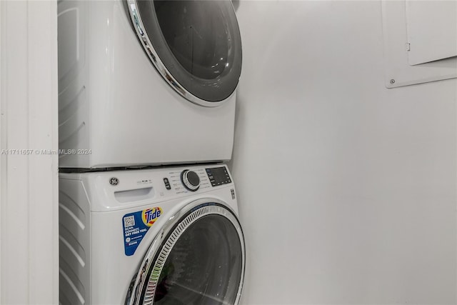 clothes washing area with electric panel and stacked washer and clothes dryer