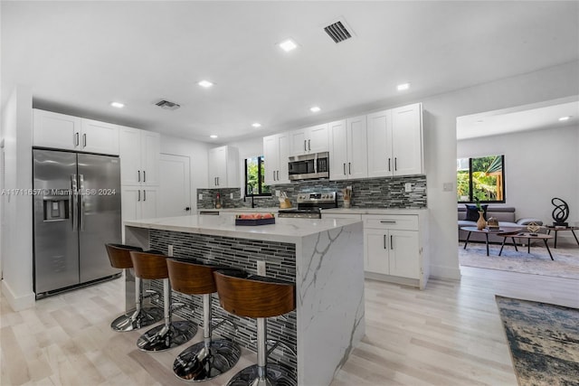 kitchen featuring white cabinets, a breakfast bar area, appliances with stainless steel finishes, and light hardwood / wood-style flooring