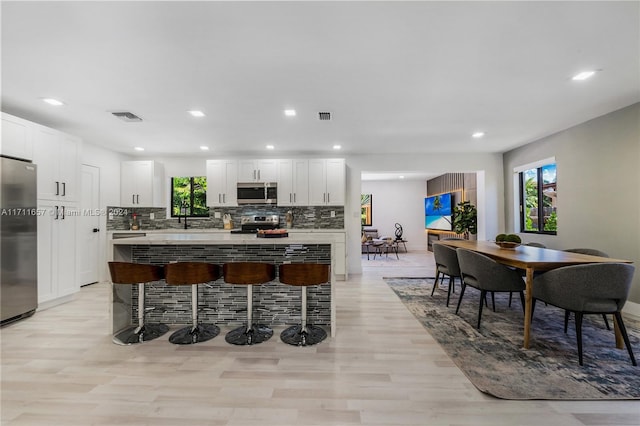 kitchen featuring stainless steel appliances, tasteful backsplash, light hardwood / wood-style flooring, a breakfast bar area, and white cabinets