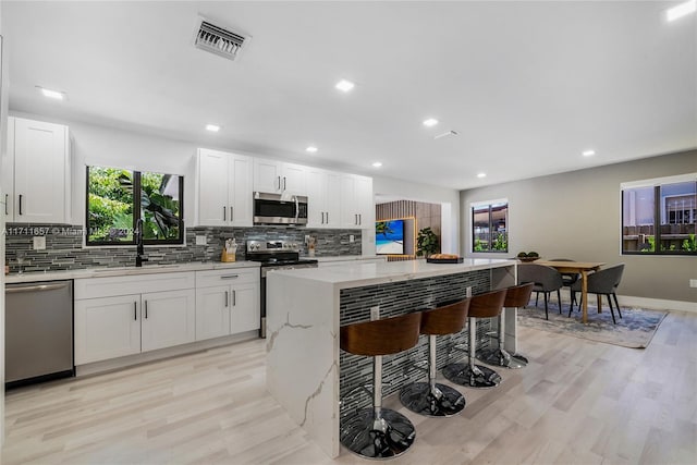 kitchen featuring light stone countertops, stainless steel appliances, white cabinetry, and light hardwood / wood-style floors