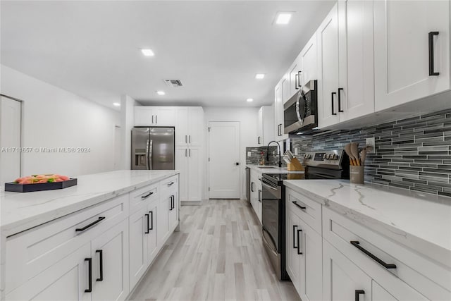 kitchen featuring white cabinets, light stone countertops, appliances with stainless steel finishes, and light hardwood / wood-style flooring