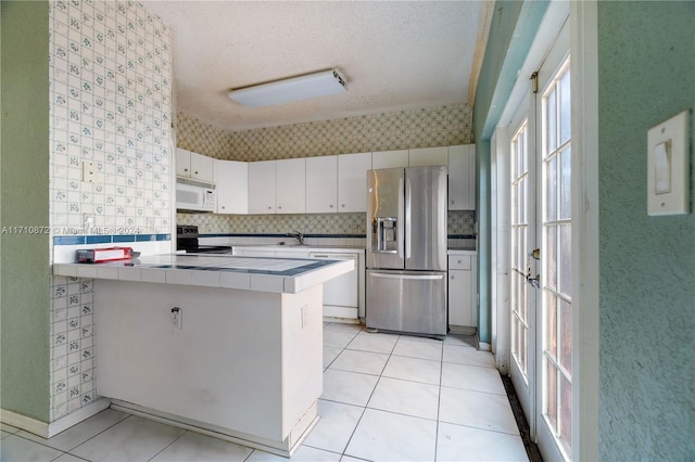 kitchen with kitchen peninsula, a textured ceiling, tile counters, white cabinetry, and stainless steel appliances