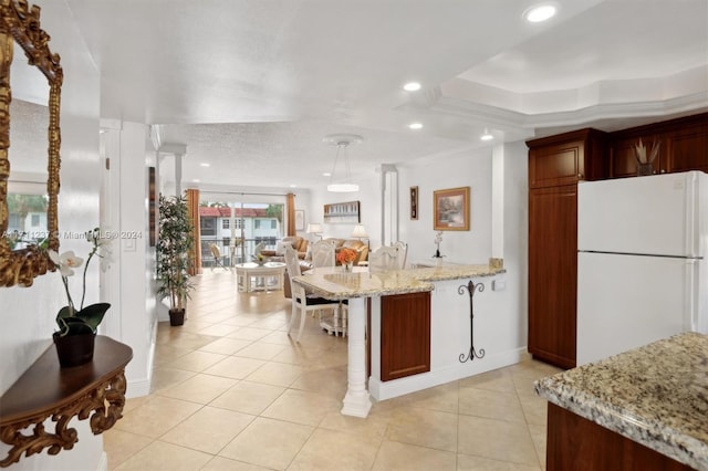 kitchen featuring ornamental molding, white refrigerator, light stone counters, a tray ceiling, and light tile patterned flooring