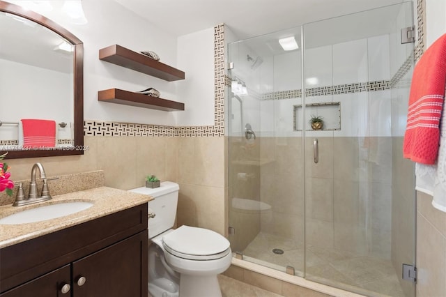 bathroom with tile walls, toilet, a shower with shower door, and vanity