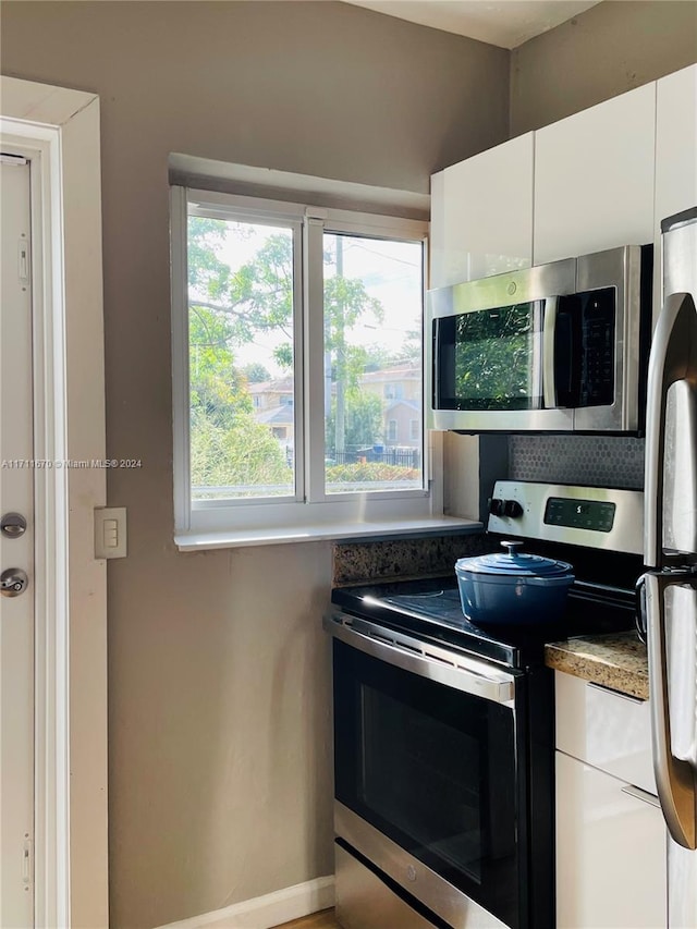 kitchen with tasteful backsplash, white cabinets, and appliances with stainless steel finishes