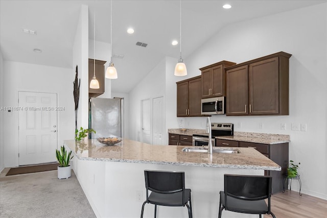 kitchen with a kitchen breakfast bar, light stone counters, stainless steel appliances, vaulted ceiling, and hanging light fixtures