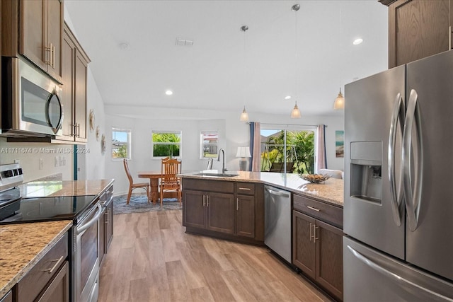 kitchen featuring appliances with stainless steel finishes, light stone counters, sink, pendant lighting, and light hardwood / wood-style floors