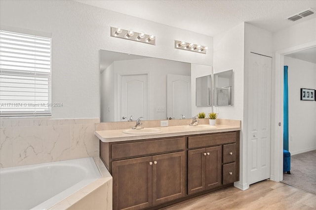 bathroom with hardwood / wood-style flooring, vanity, a textured ceiling, and tiled bath