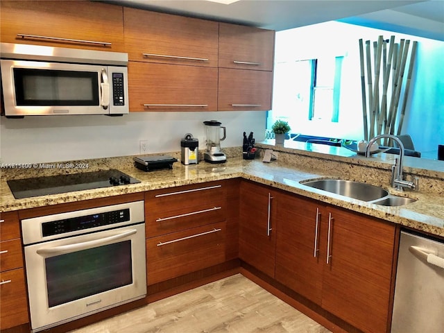 kitchen with light stone countertops, light wood-type flooring, sink, and appliances with stainless steel finishes