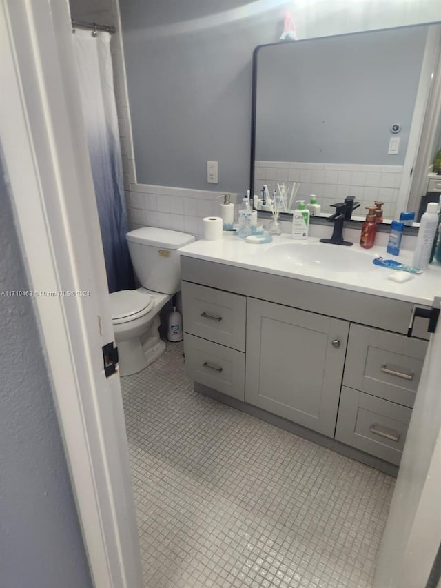 bathroom featuring tile patterned flooring, vanity, tile walls, and toilet