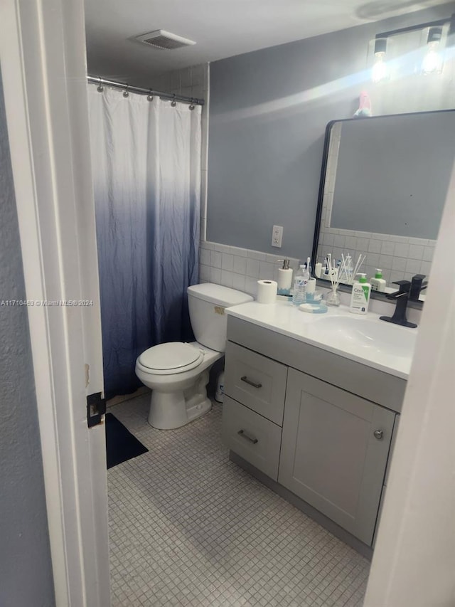 bathroom featuring tile patterned floors, vanity, tile walls, and toilet