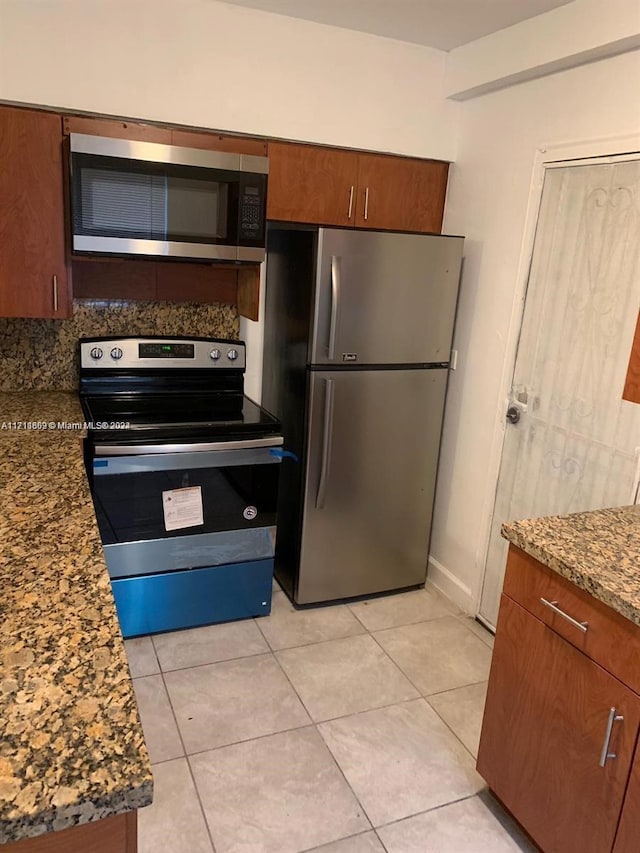 kitchen featuring appliances with stainless steel finishes, dark stone counters, and light tile patterned flooring