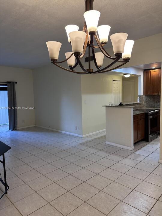 kitchen with tasteful backsplash, a notable chandelier, kitchen peninsula, pendant lighting, and light tile patterned floors