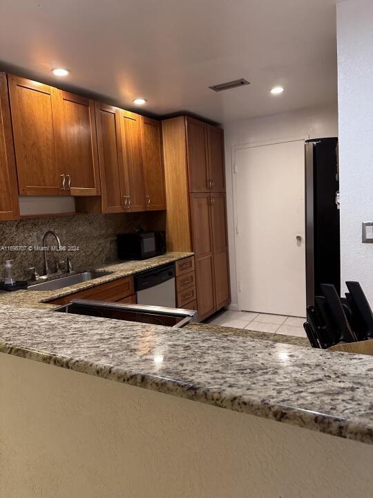 kitchen with sink, dishwasher, light stone counters, backsplash, and light tile patterned floors