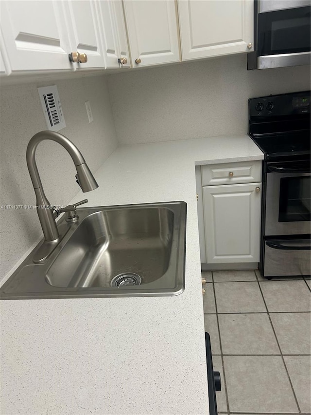 kitchen with black / electric stove, sink, white cabinets, and light tile patterned floors