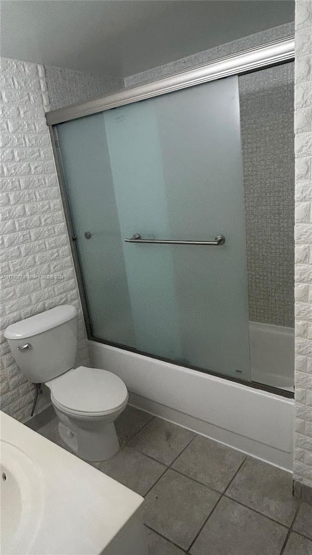 bathroom with tile patterned flooring, toilet, and bath / shower combo with glass door