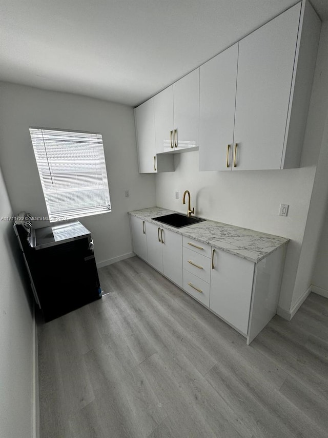 kitchen featuring white cabinetry, sink, light stone countertops, and light wood-type flooring