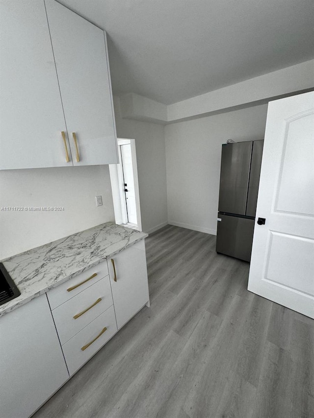 kitchen featuring stainless steel fridge, light wood-type flooring, white cabinetry, and light stone counters