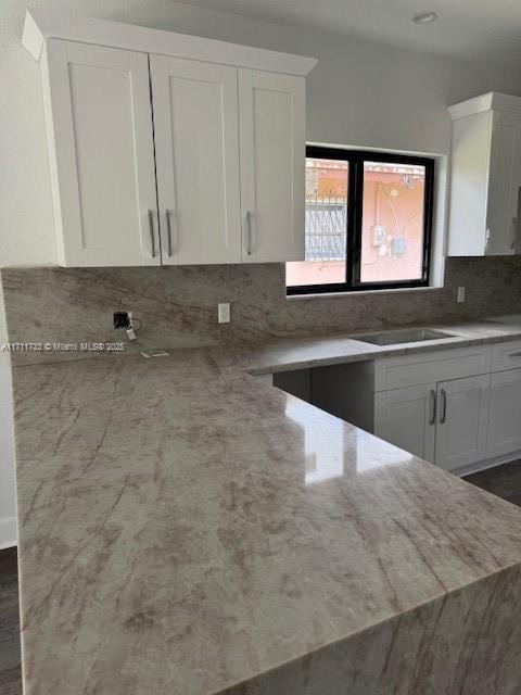 kitchen with light stone countertops, a sink, white cabinets, and decorative backsplash