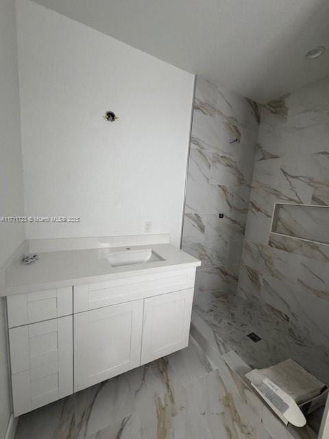 bathroom featuring a tile shower, marble finish floor, and vanity