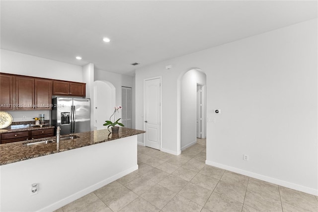 kitchen featuring stainless steel fridge with ice dispenser, sink, light tile patterned floors, and dark stone counters