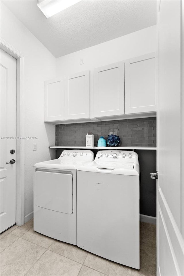 laundry area with cabinets, light tile patterned floors, a textured ceiling, and washing machine and clothes dryer