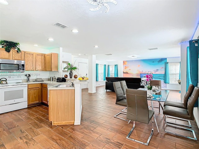 kitchen with sink, white electric range oven, kitchen peninsula, a kitchen bar, and hardwood / wood-style flooring