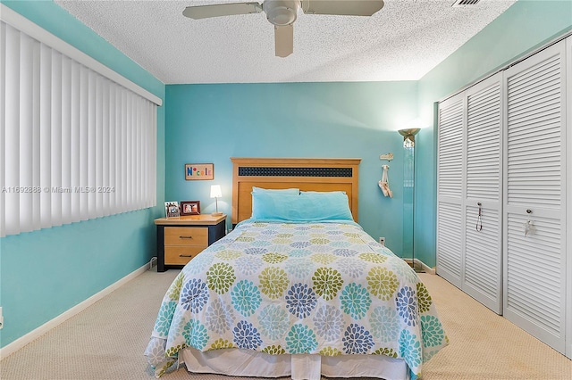 bedroom with ceiling fan, a textured ceiling, light carpet, and a closet