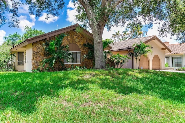 view of front of property featuring stone siding, a tiled roof, a front lawn, and stucco siding